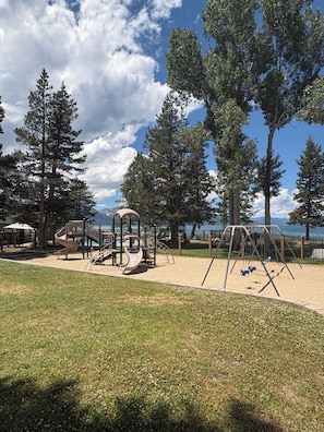 A playground with slides and swings, surrounded by trees and a view of the water. - Tahoe Keys Studio Retreat - HOA Amenities (South Lake Tahoe)