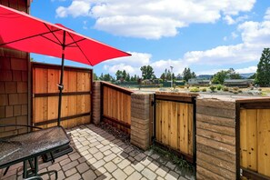 Un espace patio avec un parasol rouge, une table et une vue sur un quartier résidentiel.