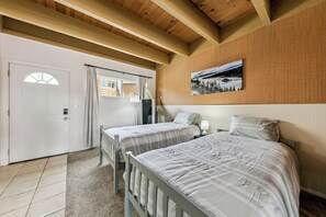 Ein Zimmer mit zwei Betten, einer Holzbalkendecke, einem Bild an der Wand und einer Tür mit Fenster.