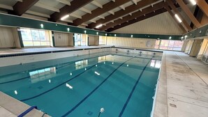 Une piscine intérieure avec des couloirs bien délimités, un sol carrelé et un plafond haut avec des poutres en bois.