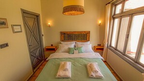 A hotel room with a bed, two nightstands, a wooden headboard, a window, and a door.