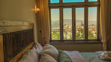 Une chambre avec un lit, une fenêtre donnant sur un paysage urbain et un luminaire fixé au mur.