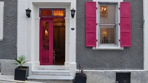 A building with a white facade, a red door, and pink shutters.