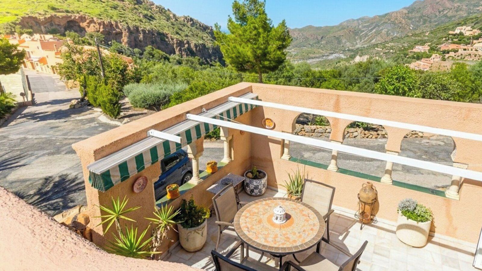 A patio with a round table, chairs, potted plants, and a view of a mountainous landscape.