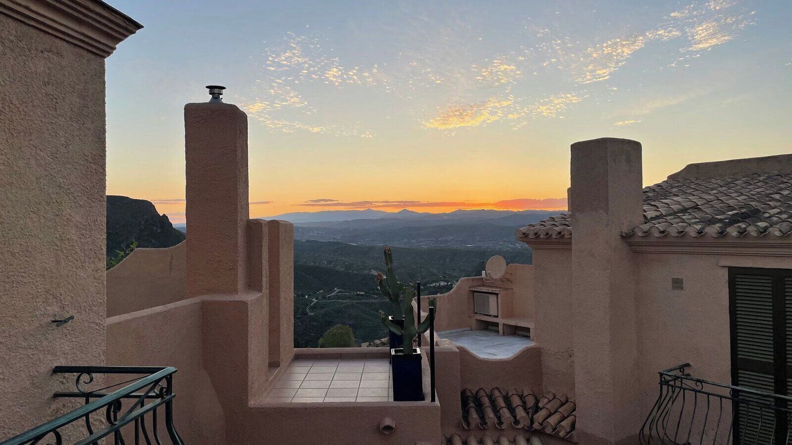 A balcony with a view of a mountainous landscape during sunset.