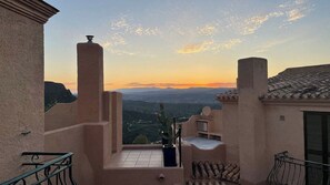 A balcony with a view of a mountainous landscape during sunset.