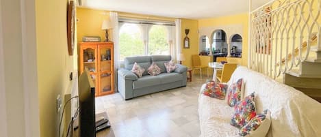 A living room with a sofa, a television, a cabinet, and a dining area with a table and chairs.
