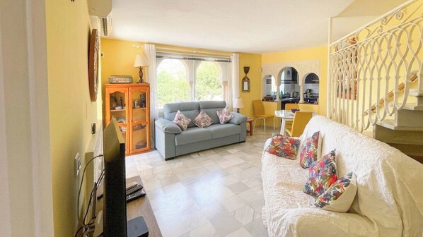 A living room with a sofa, a television, a cabinet, and a dining area with a table and chairs.