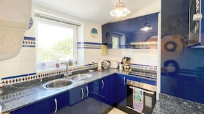 A kitchen with blue cabinets, a double sink, and a window with decorative tiles.