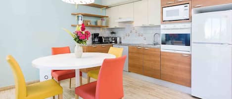 Una cocina moderna con una mesa de comedor redonda, sillas coloridas y un refrigerador blanco.