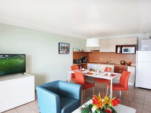 A modern kitchen with white cabinets, a dining table set for four, and a television displaying a sports game. - Minutes from Maho Beach and Mullet Bay Beach (Maho Bay)