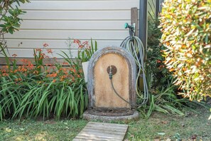 Ein Gartenschlauch, verbunden mit einem verwitterten, hölzernen Außenwasserhahn.