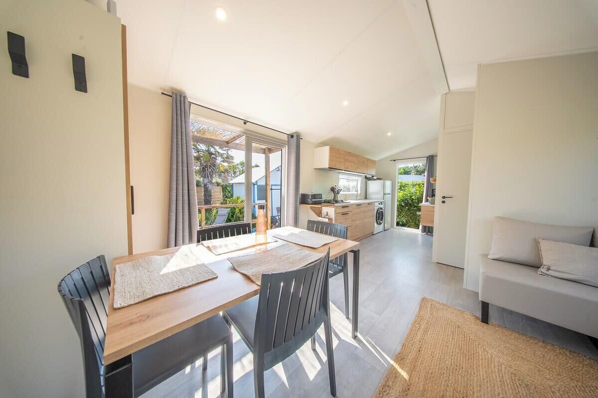 A modern kitchen with a dining area, a sofa, and a view of greenery.