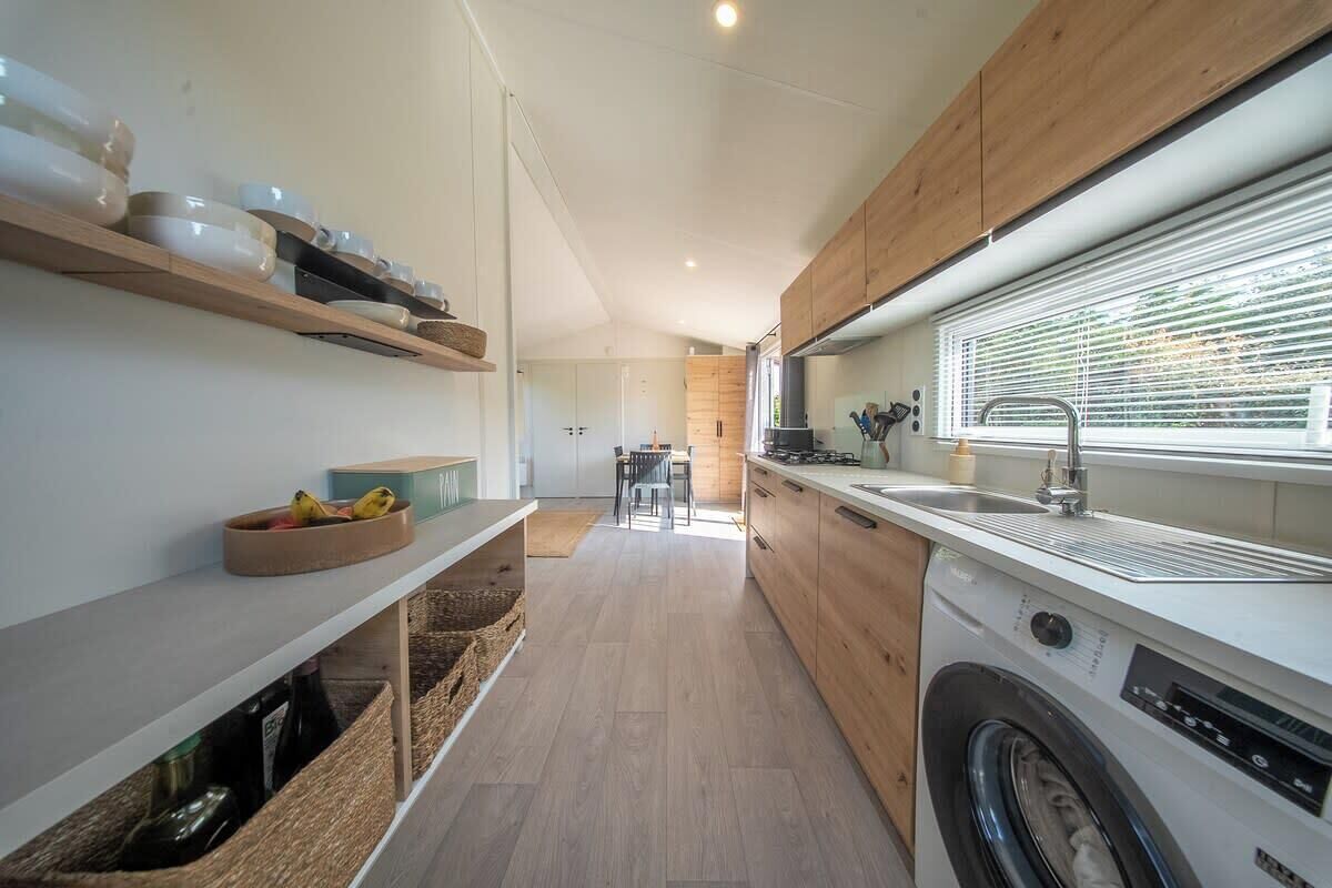 A compact kitchen with a washing machine, wooden cabinets, and a window with blinds.