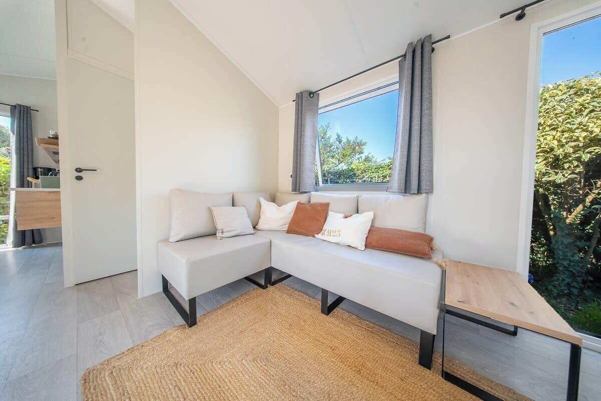 Un salon moderne avec un canapé d’angle, une petite table en bois et une vue sur la verdure à l’extérieur.
