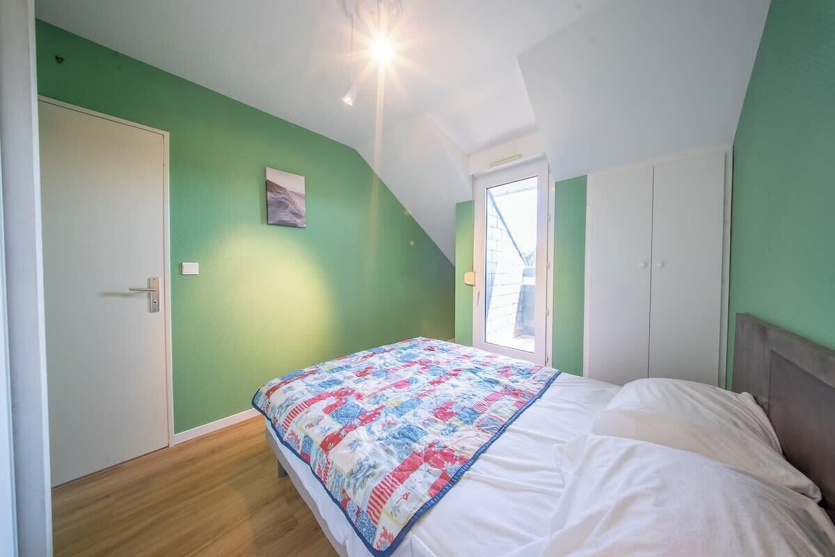 Un dormitorio con techo inclinado, una cama con colcha colorida, una puerta y una ventana.