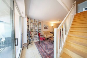 Eine Treppe führt zu einer Empore mit einem Bücherregal, einem roten Sessel und einem gemusterten Teppich.