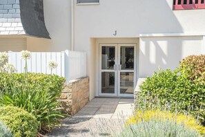 A white building with a glass door entrance, a stone wall, and a white fence. - Grand Appartement Familial Vue Port avec Piscine (Arzon)