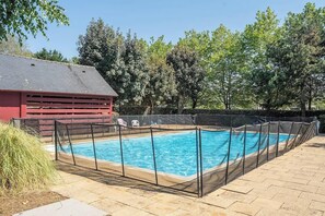 A rectangular swimming pool with a safety fence, surrounded by a paved patio area. - Grand Appartement Familial Vue Port avec Piscine (Arzon)
