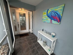 A hallway with a door, a console table with a 'Welcome' sign, a colorful painting, and a tiled floor. - Pool, Sunsets and Water Access! 3-bedroom house in lovely Cape Coral (Cape Coral)