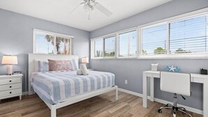 Une chambre à coucher avec un lit, des tables de chevet, un bureau et un ventilateur de plafond.