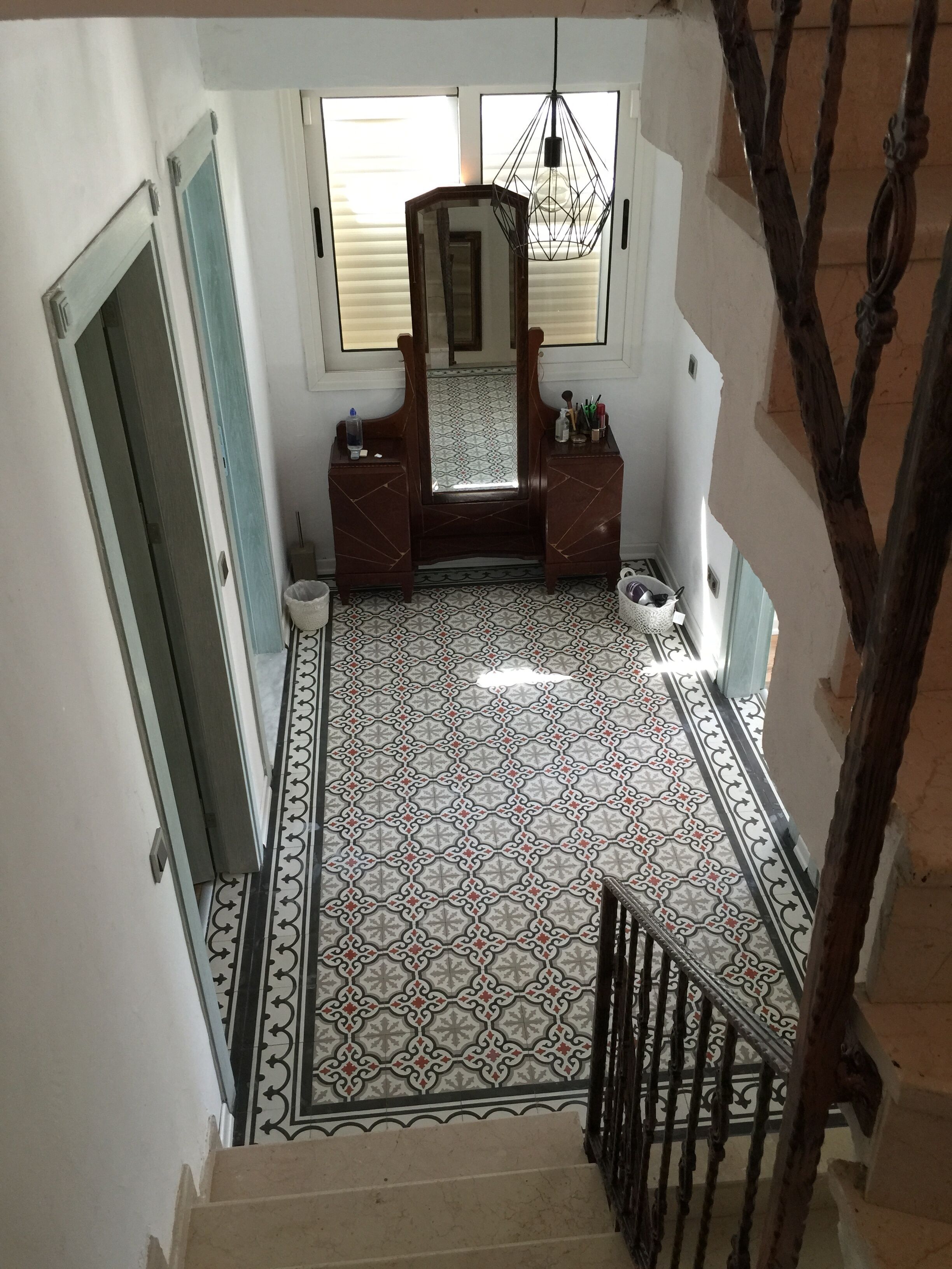 A staircase leading to a room with a patterned floor, a mirror, and a hanging light fixture.