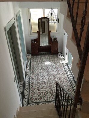 A staircase leading to a room with a patterned floor, a mirror, and a hanging light fixture.