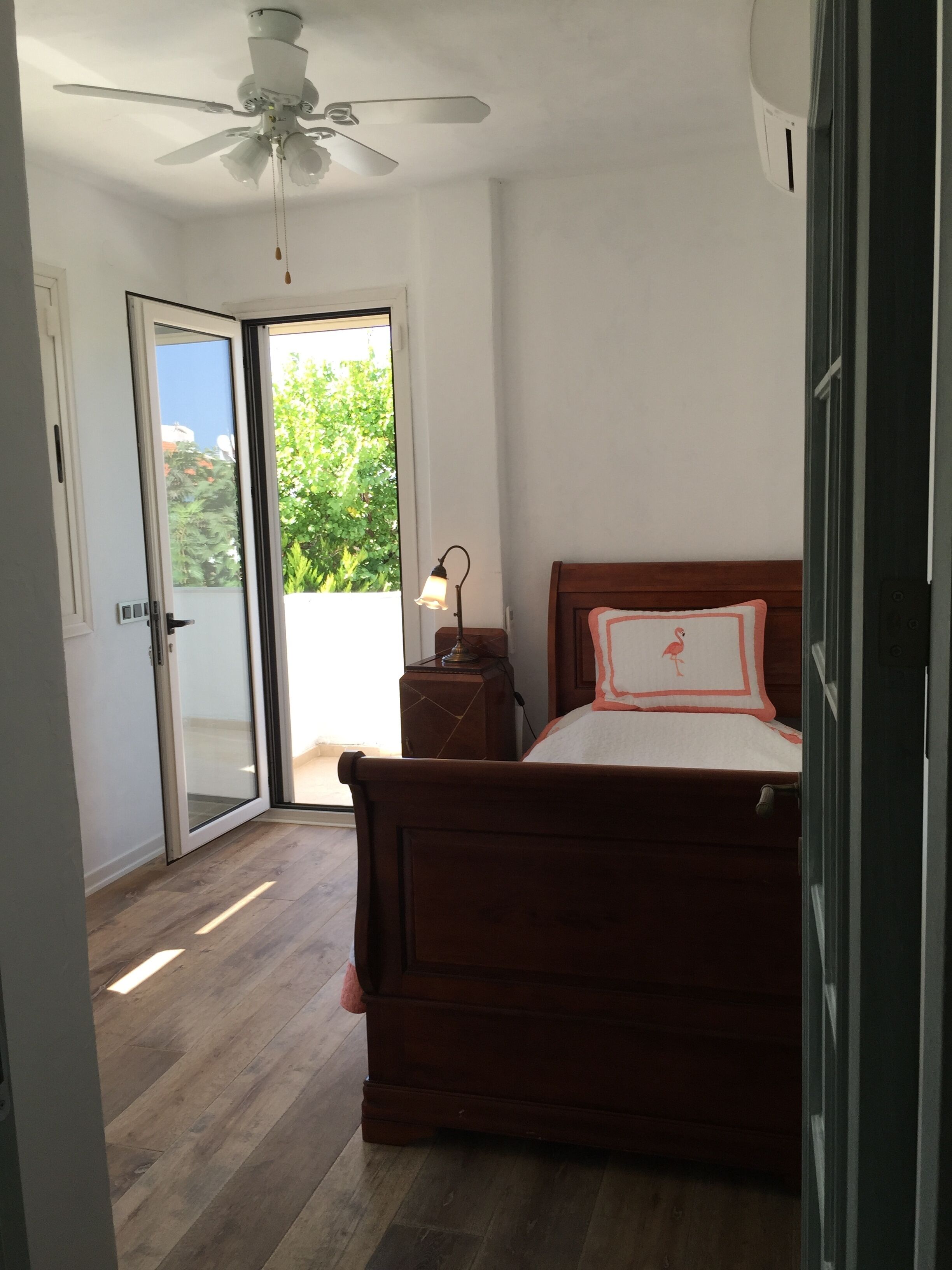 A bedroom with a wooden bed, a nightstand, a ceiling fan, and a sliding glass door leading to a balcony.