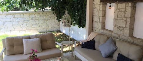 A cozy outdoor seating area with two sofas, a glass coffee table, and a decorative birdcage.