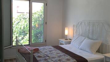A bedroom with a bed, a nightstand, a lamp, a ceiling fan, and a window with a view of greenery.