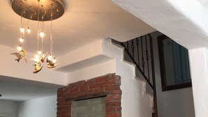 A staircase with a brick wall and a green door, a chandelier with hanging lights, and a television in the background. - Spacious 4-bedroom home-sleeps 9 with AC in all rooms-3 minutes from the sea! (Çeşme)