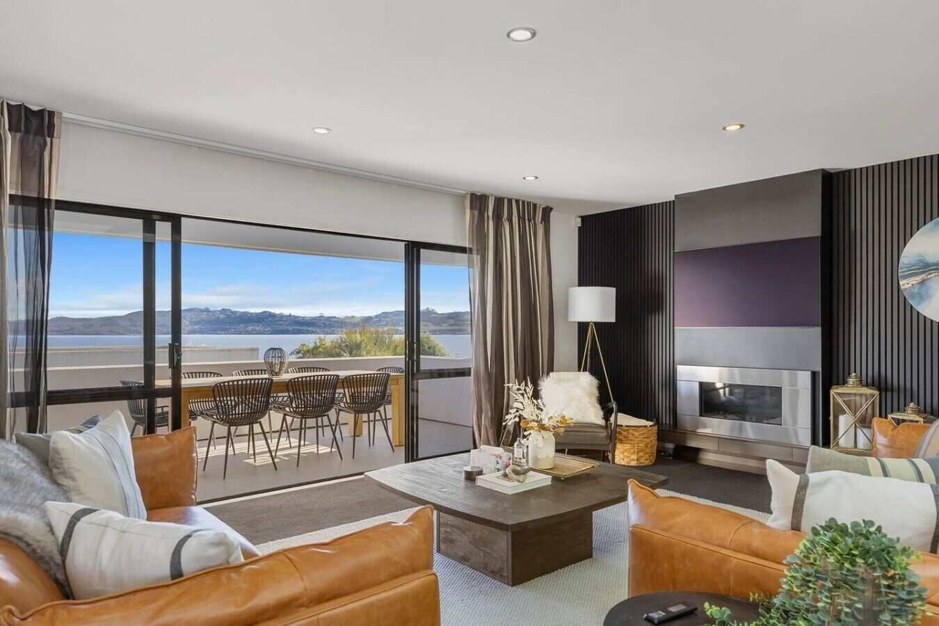 A modern living room with a fireplace, leather sofas, a dining area with chairs, and a large window overlooking a scenic view.