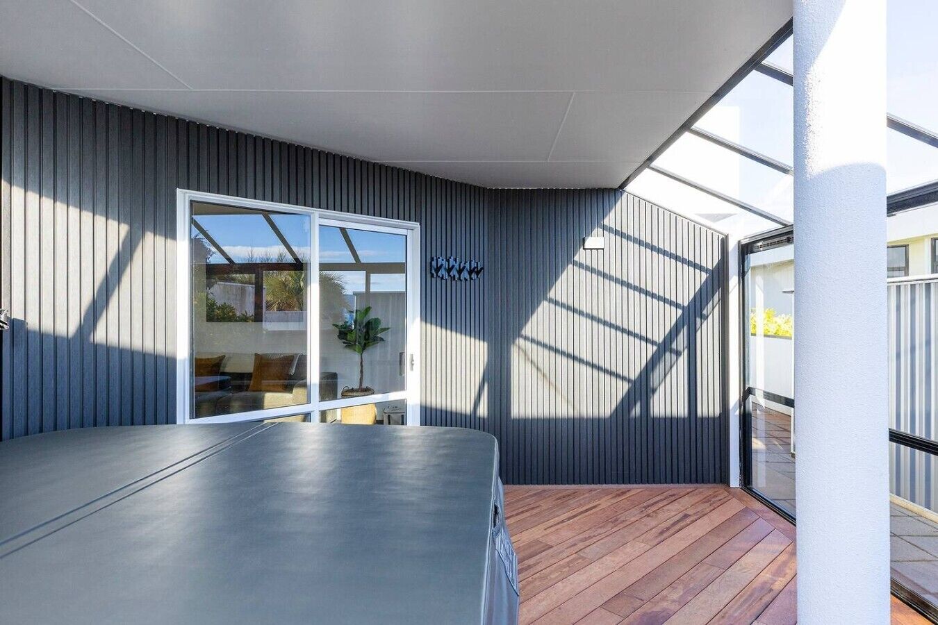Un patio moderno al aire libre con un piso de madera, una puerta corrediza de vidrio que da a una sala de estar y una baranda de metal.
