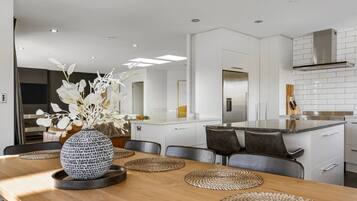 A modern kitchen with white cabinetry, a stainless steel range hood, and a dining area with a wooden table and woven placemats.