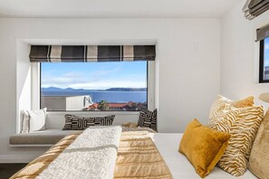 A bedroom with a large window, a bed with multiple pillows, and a view of the sea. - Harvey Heights Retreat (Taupō)