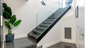 Un interior moderno con una escalera de vidrio, una planta en maceta y una rejilla de ventilación.