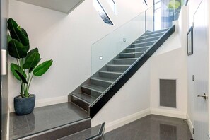 A modern interior with a glass staircase, a potted plant, and a vent. - Harvey Heights Retreat (Taupō)