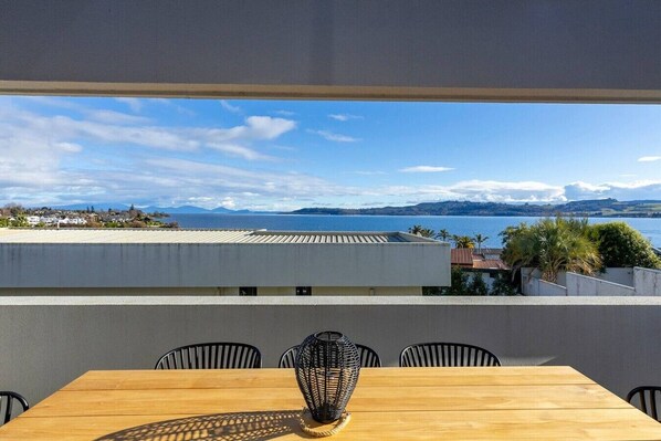 Ein Essbereich mit Blick auf Meer und Berge, ein Holztisch und schwarze Stühle.