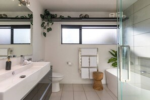 Ein modernes Badezimmer mit einem großen Spiegel, einem weißen Waschbecken, einer Toilette und einer Duschkabine aus Glas.