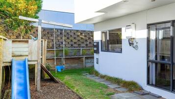A modern outdoor play area with a slide, a swing, and a climbing structure.