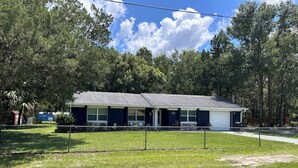 A single-story house with a dark blue exterior, a front porch, and a fenced yard. - Homosassa Getaway 3/2 (Homosassa)