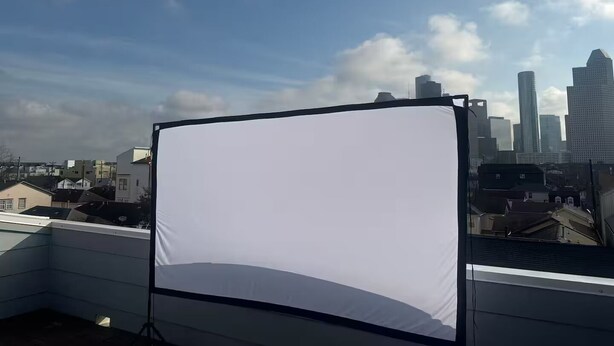 Eine Dachterrasse mit einer weißen Leinwand, im Hintergrund ein Stadtbild und ein klarer Himmel.