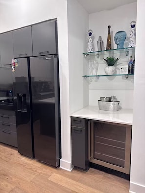 Eine moderne Küche mit einem schwarzen Kühlschrank, einer Mikrowelle, einem Spülbecken und einer Glasablage mit Weingläsern und Flaschen.