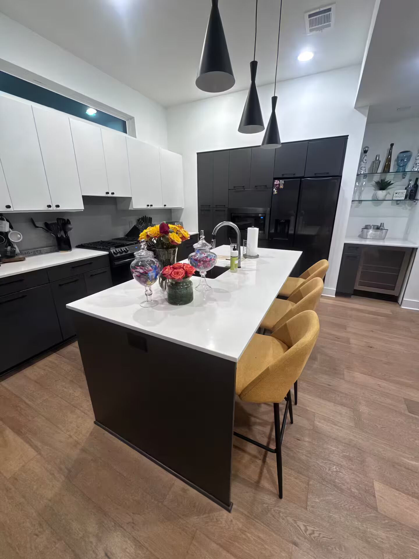 Une cuisine moderne avec des meubles blancs et noirs, un îlot central doté de chaises et des luminaires suspendus.