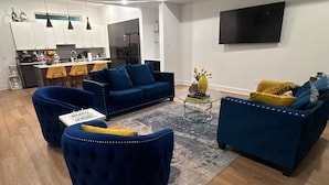 Ein modernes Wohnzimmer mit Deckenventilator, Flachbildfernseher an der Wand und einer Küchenzeile im Hintergrund.