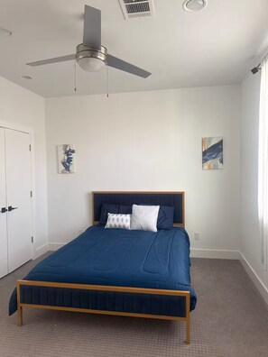 A bedroom with a bed, a ceiling fan, a door, and a painting on the wall.