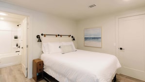 A bedroom with a bed, bedside table, lamp, and a painting on the wall. - Rooftop Patio Downtown GH: Steps to Lake & Dining (Grand Haven)