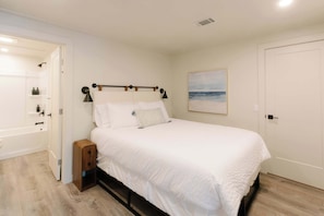 Un dormitorio con cama, mesita de noche, lámpara y un cuadro en la pared.