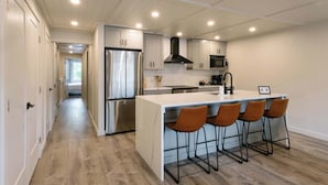 A modern kitchen with a stainless steel refrigerator, a microwave, and a large island with bar stools. - Rooftop Patio Downtown GH: Steps to Lake & Dining (Grand Haven)