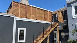 A residential building with a wooden deck, a staircase, and a grey exterior wall. - Rooftop Patio Downtown GH: Steps to Lake & Dining (Grand Haven)